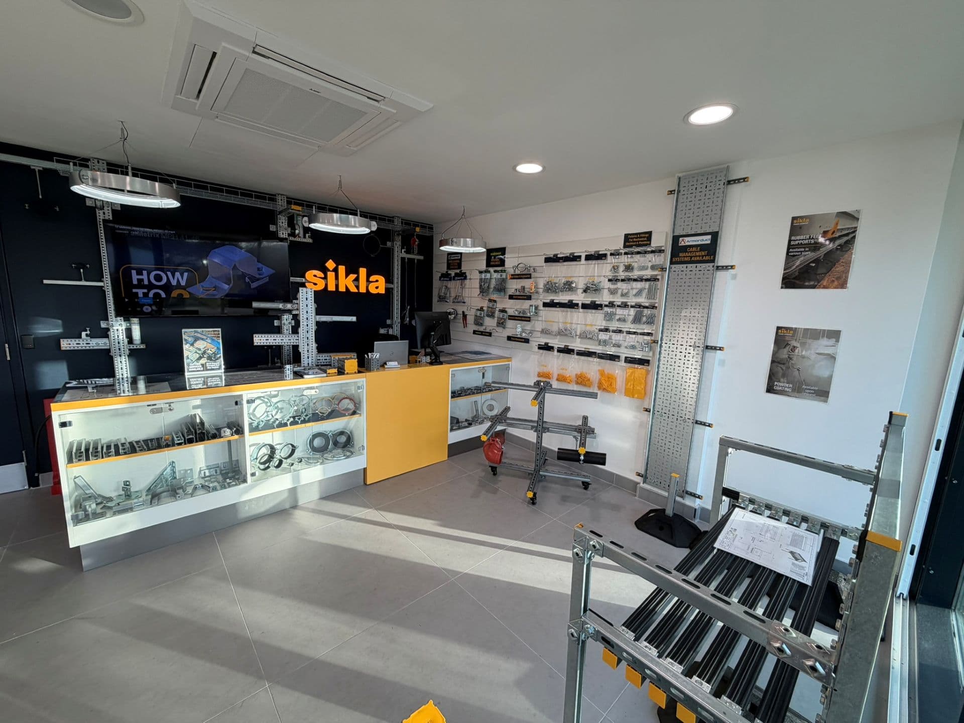 Modern showroom counter with yellow-accented glass display cases,  metal fittings and 'sikla' illuminated logo behind the desk.