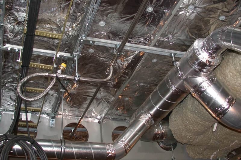 Industrial ceiling with reflective insulation, metal vents, and wiring. Ductwork wrapped in insulation material visible in the foreground.